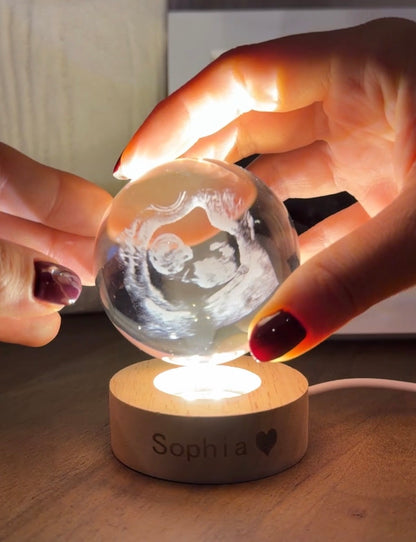 Glass ball with ultrasound image on a wooden base, held by a person with an ultrasound photo in the background.